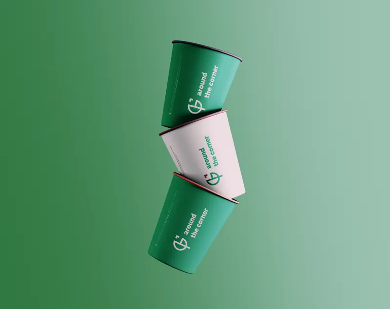 Around the Corner brand on three takeaway cups stacked against a green field.